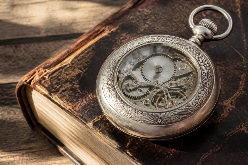 A close-up photograph of a vintage American pocket watch with intricate engravings, resting on a worn leather-bound book, with soft natural light highlighting the craftsmanship