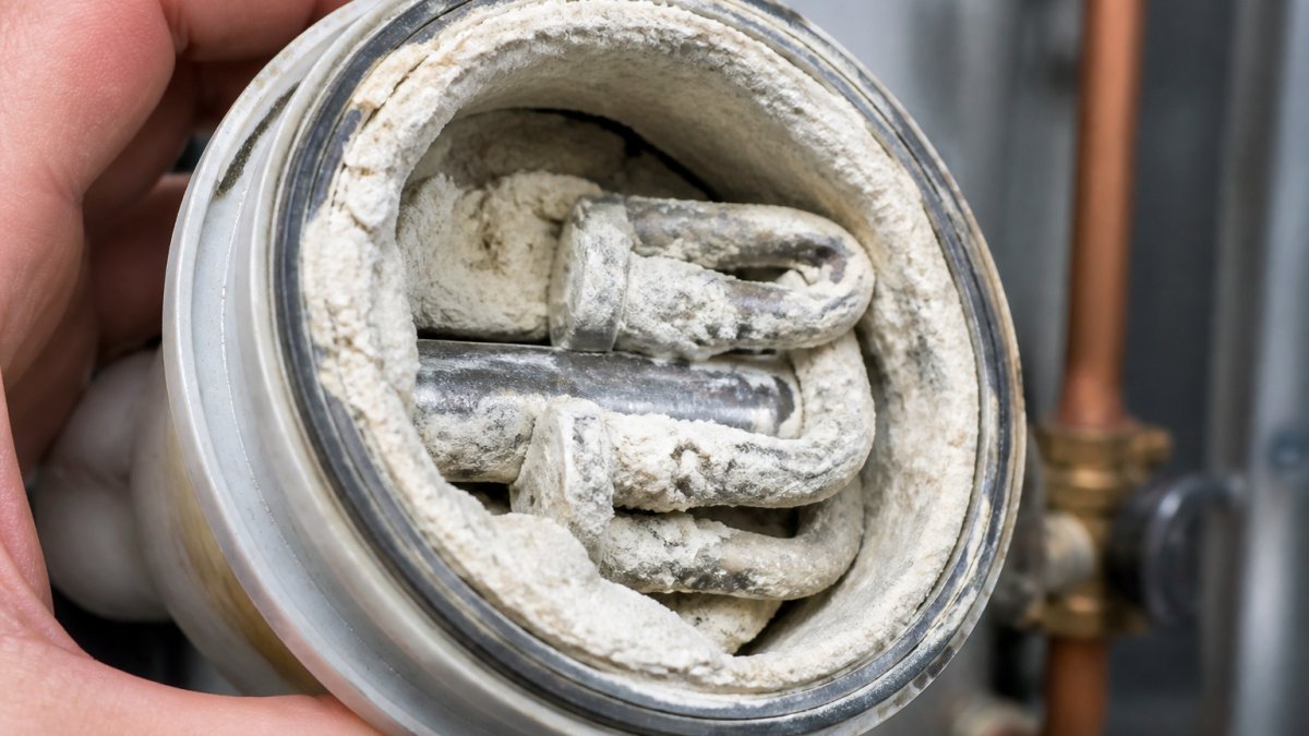 Close-up of white mineral scale and calcium deposits coating the interior of a water heater element or copper pipe fitting, showing thick buildup caused by hard water