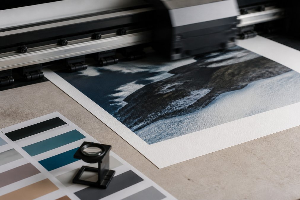 Close-up of a large-format printer applying ink to textured paper during the professional giclée printing process.