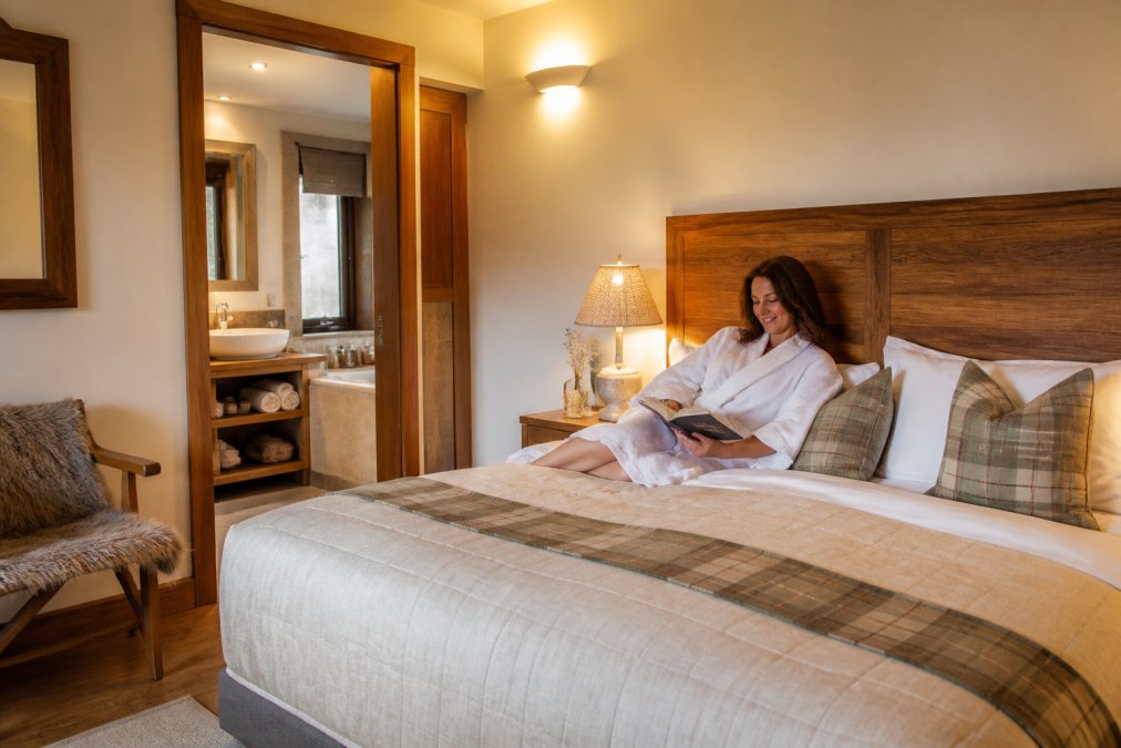 Guest relaxing in a comfortable, elegantly appointed bedroom at a luxury lodge, featuring handmade furnishings, ensuite bathroom, and warm, inviting lighting that suggests comfort and personalized hospitality