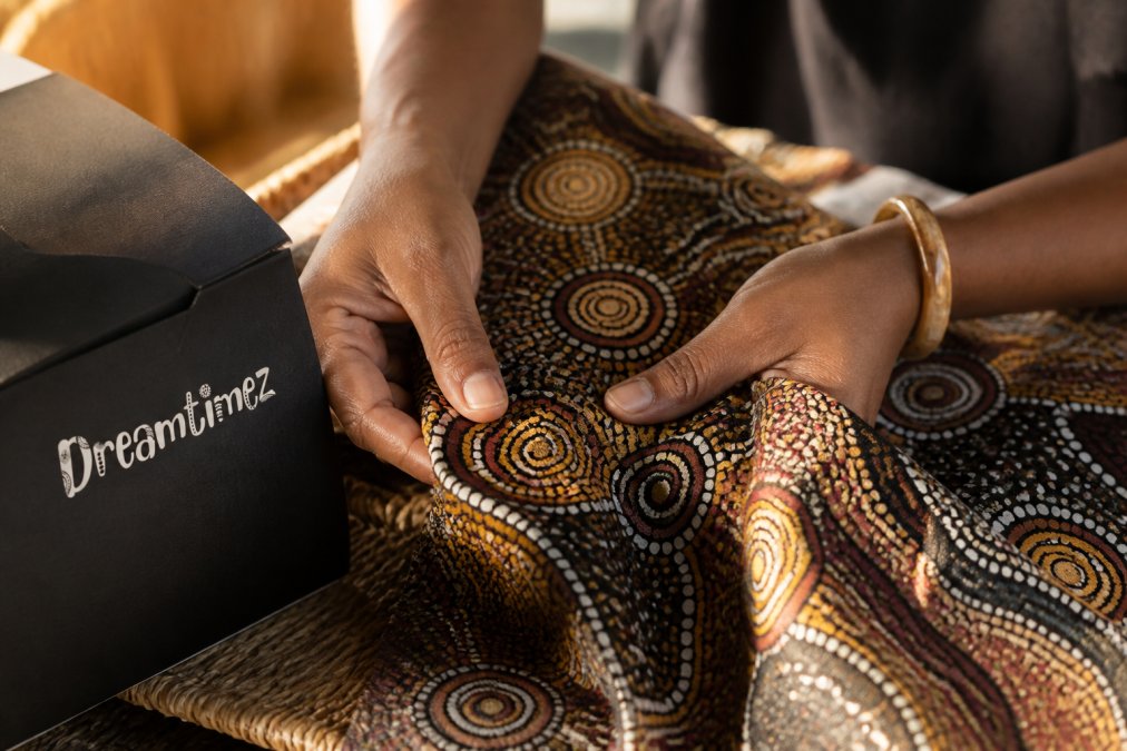 Close-up of hands carefully examining a piece of authentic Indigenous textile or artwork, showing intricate traditional patterns and natural fibres under warm natural light