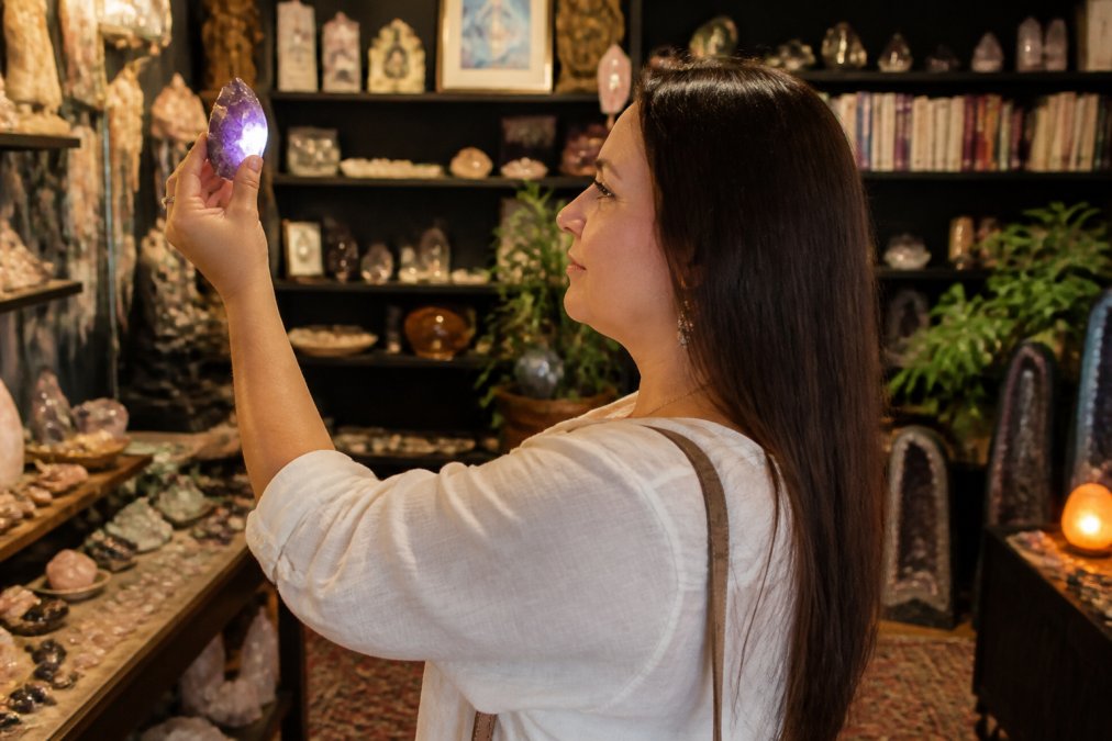 Person examining a crystal in a local metaphysical shop filled with books and stones