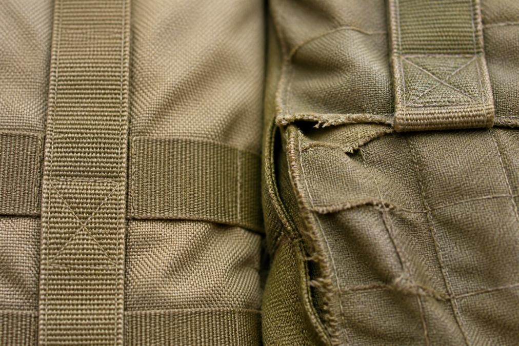 Close-up of tactical backpack fabric showing reinforced stitching detail, seam construction, and material texture with visible quality differences between dense weave and fraying edges