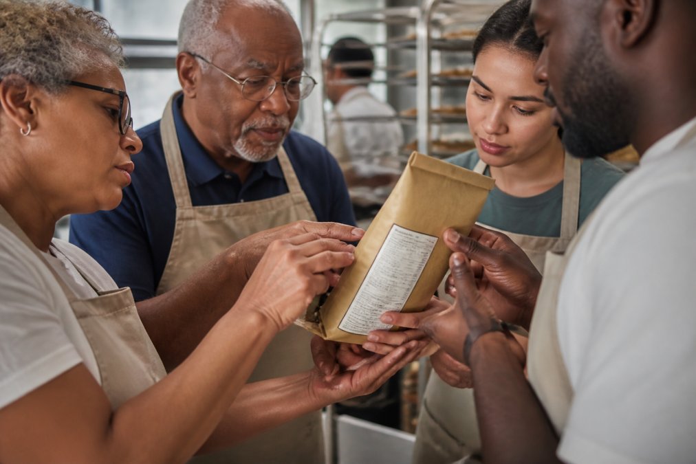 Close-up of hands of different skin tones examining a food product package together, carefully reading labels and certification details on the packaging