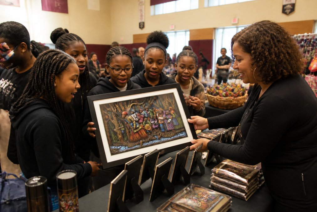 Students and community members gathered examining culturally inspired gifts and products, showing excitement and engagement with Black-owned merchandise in a bright community center