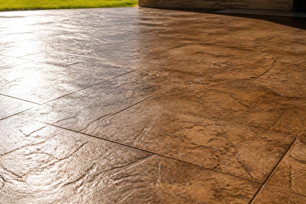 Close-up of decorative concrete patio surface showing texture and finish quality, with sunlight highlighting the surface texture, color variations, and protective sealant sheen