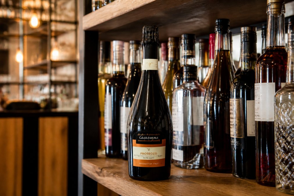 Close-up of premium wine and spirit bottles arranged on shelves in a modern bar setting, with warm lighting highlighting the labels and glass
