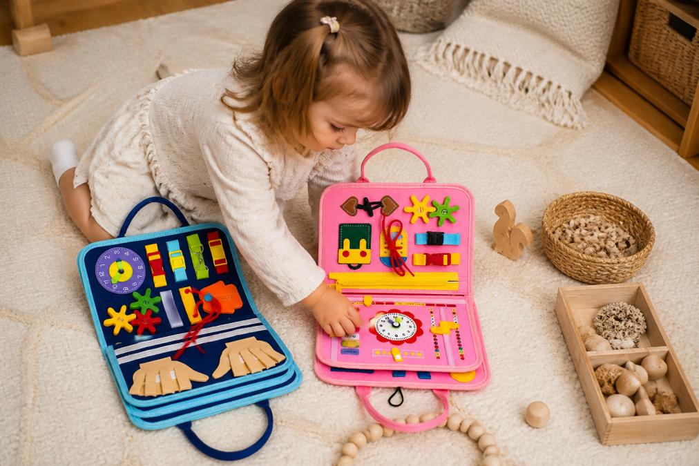 A young child exploring natural wooden toys, beaded strings, and textured materials on a neutral-coloured play mat in soft natural light, with hands actively touching and manipulating the wooden pieces