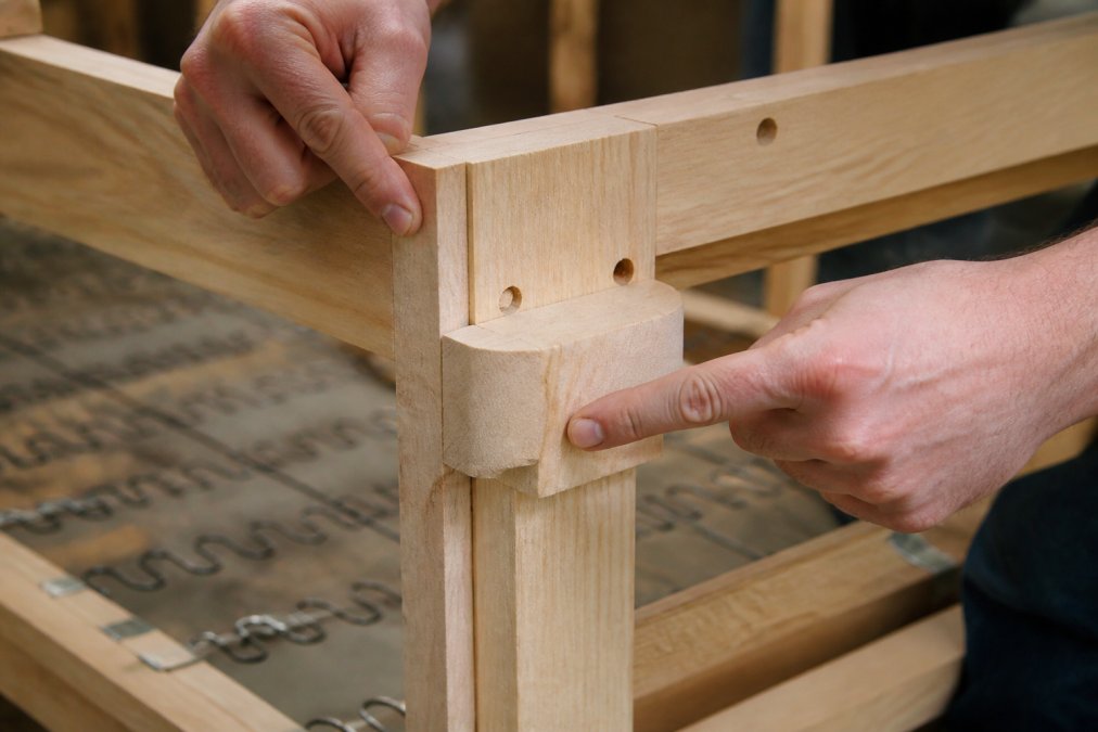 Close-up of sofa frame joints showing mortise-and-tenon construction with hands pointing to quality corner blocks and dowel joinery details
