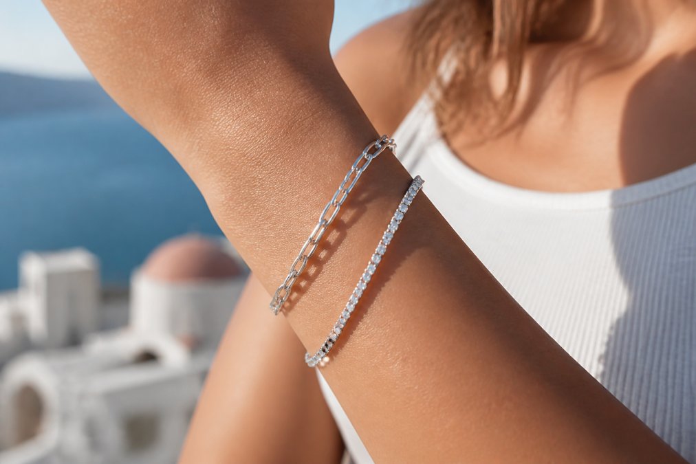 Close-up of a woman's wrist wearing a sterling silver chain link bracelet layered with a cz tennis bracelet, Mediterranean-inspired blurred background, natural sunlight catching the metal's luster