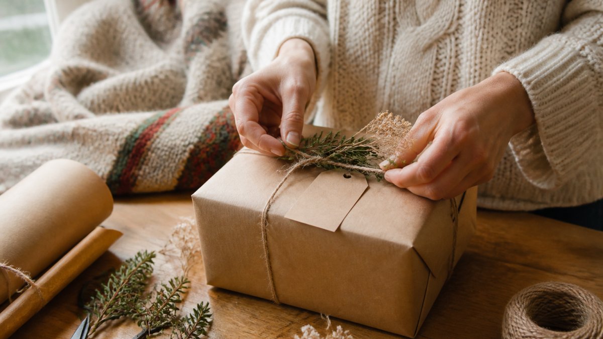 Close-up of hands wrapping a personalized gift with a handwritten note, warm natural light, cozy home setting with a woven blanket visible in the background