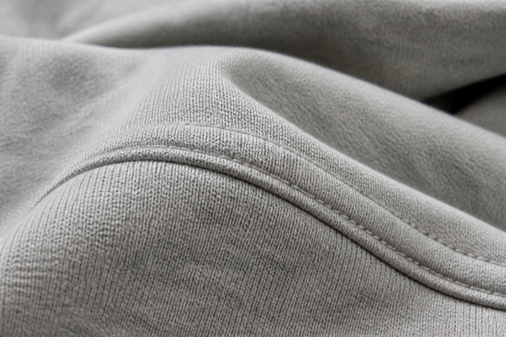 Close-up of heavyweight cotton fabric showing visible texture and weave pattern, with detailed view of double-needle stitching on a seam, natural lighting highlighting the fabric quality