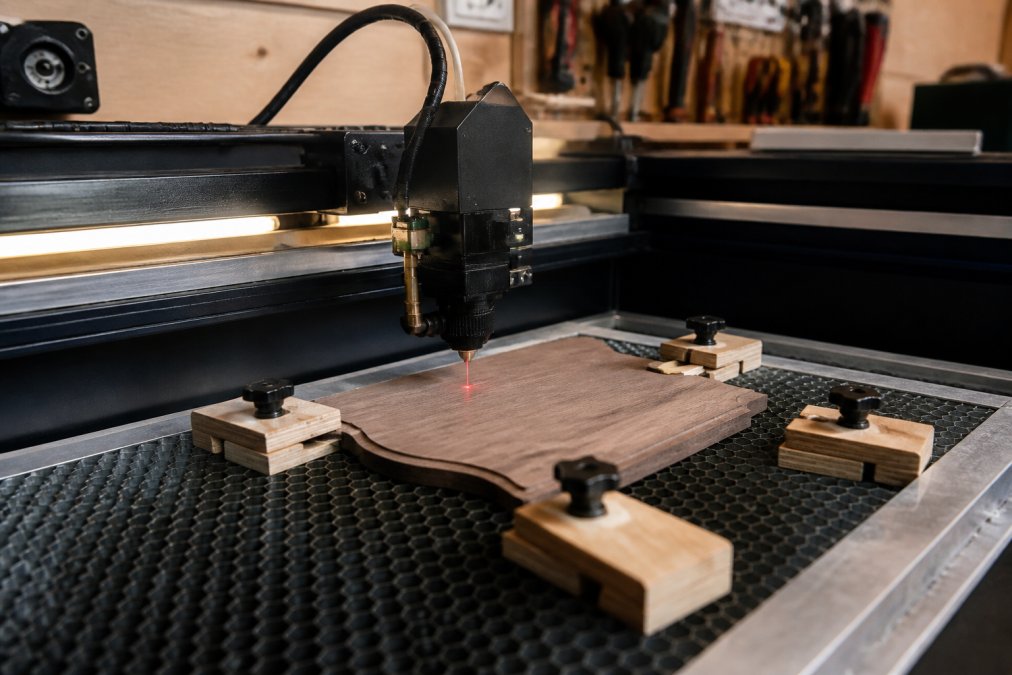 Laser beam marking a wooden plaque in a workshop, illustrating the labor behind custom engraving costs