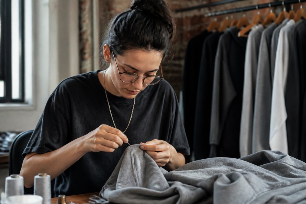 Close-up of a seamstress carefully stitching a custom garment by hand with precision needle work at a sewing station with natural lighting from a window