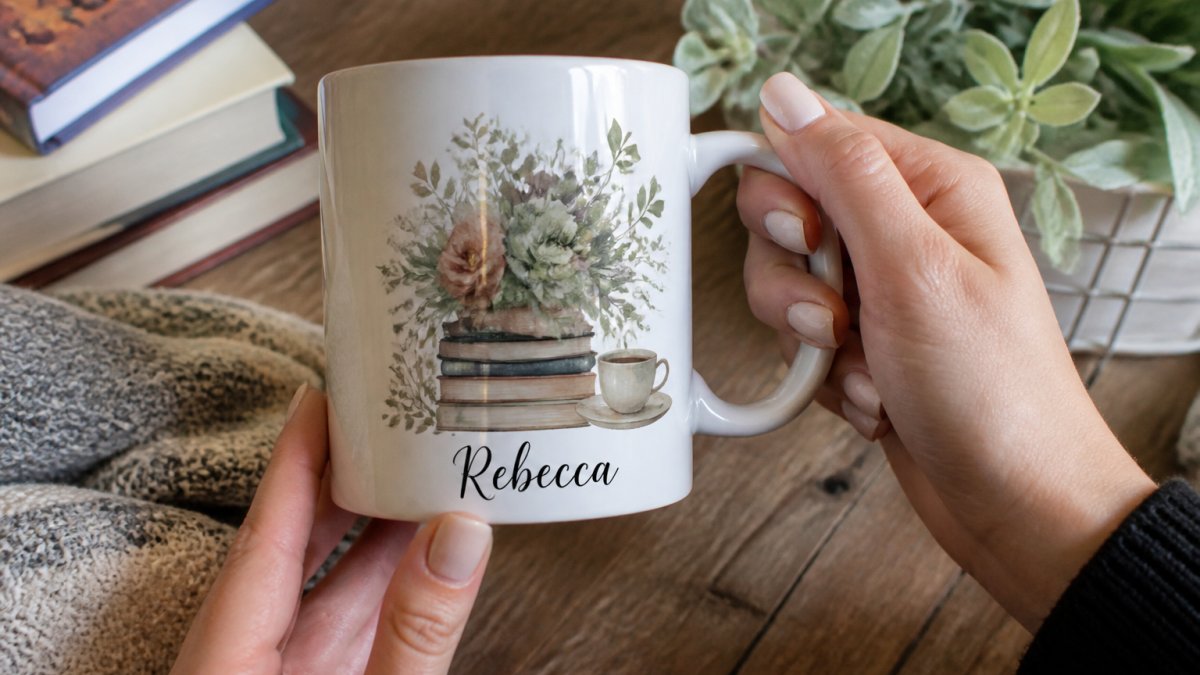 Hands holding a personalized ceramic mug with custom watercolor design and name, showing intricate detail work and quality craftsmanship on a wooden table