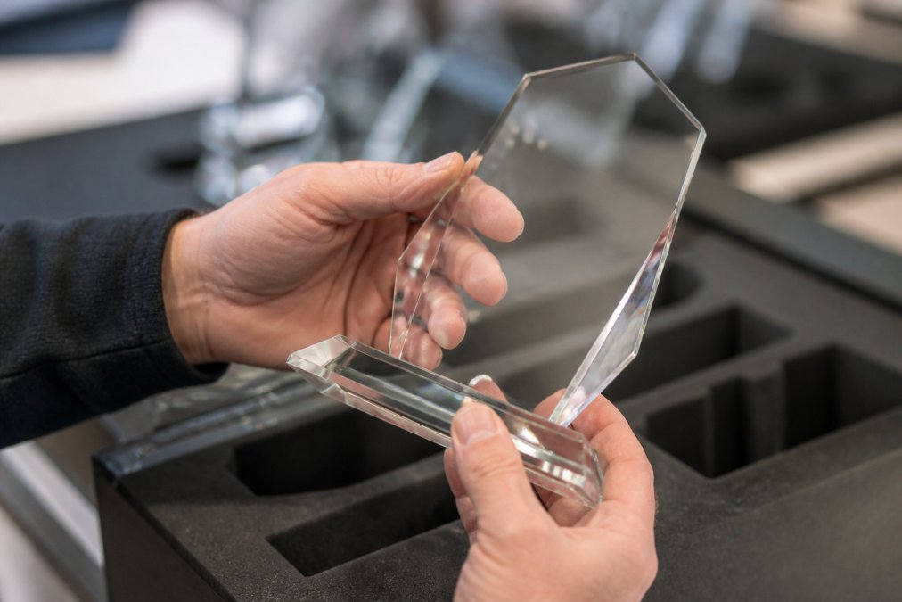 Close-up of hands examining a high-quality custom glass trophy with precise engraving, showing fine detail and craftsmanship on a polished surface