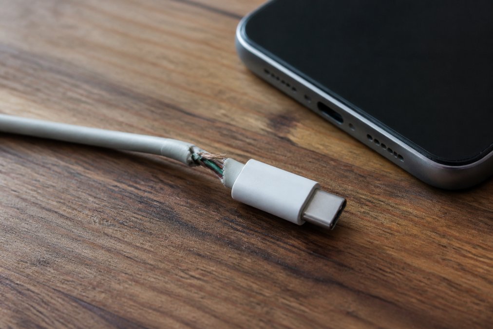 Frayed USB-C charging cable with exposed copper wires on a wooden desk, showing why charging cables fail.