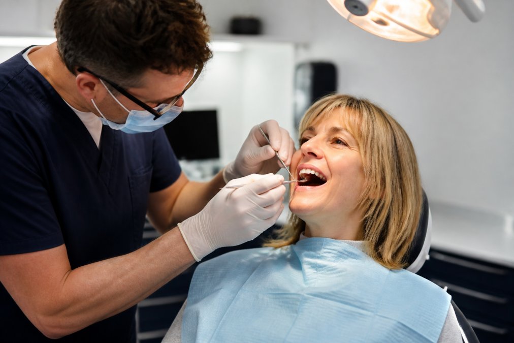 Dental professional gently examining patient's gums with an explorer tool during routine assessment in bright clinical setting with proper overhead lighting