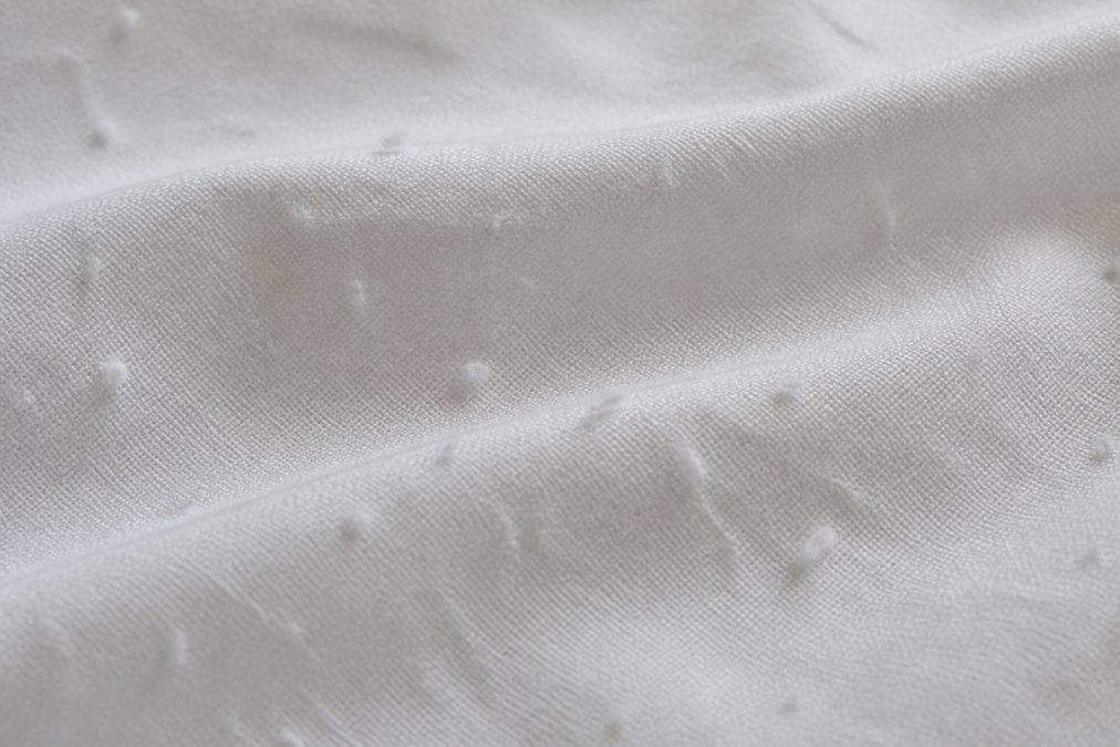 Close-up macro photograph of white bed sheet fabric showing small fuzzy pills and loose surface fibers under soft natural window light
