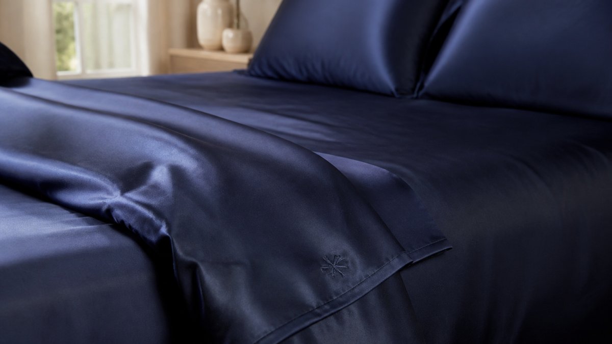 Close-up of silky navy blue bamboo viscose sheets on a neatly made bed, soft morning light catching the sateen weave and an embroidered corner size marker