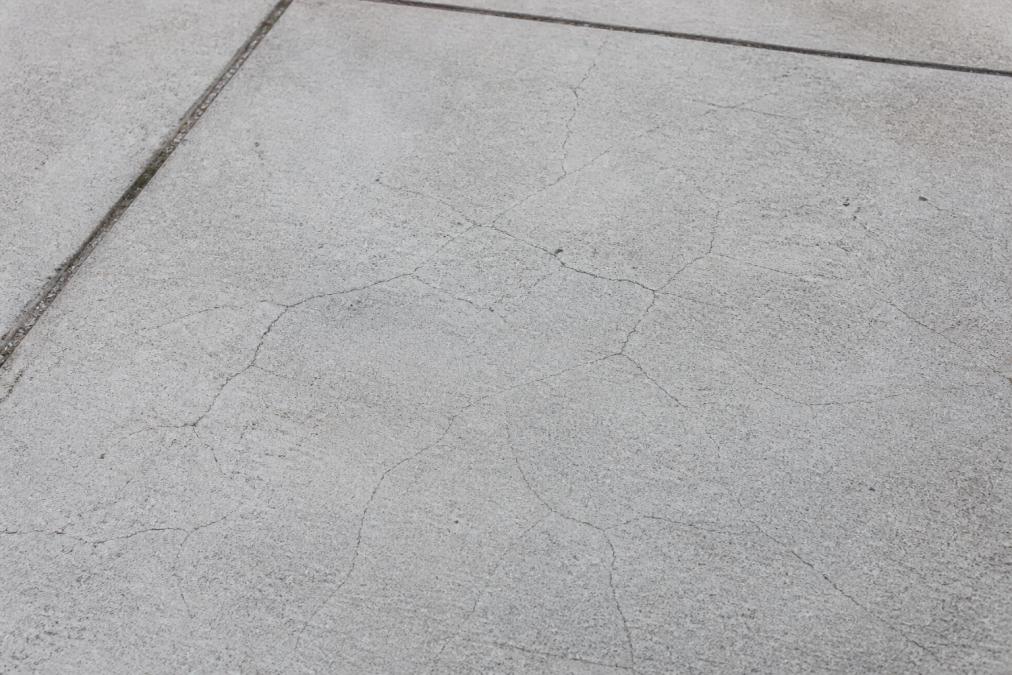 Close-up of a new concrete driveway in natural daylight showing fine, hairline surface cracks spreading in a web pattern across the slab
