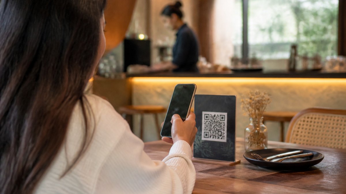 A restaurant customer scanning a branded QR code on a table tent with a smartphone, warm ambient lighting, blurred menu and staff in background
