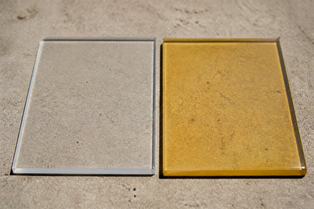 Close-up of two epoxy floor samples side by side on a concrete slab in bright natural light: one sample is glossy and crystal clear, the other is noticeably yellowed and amber-toned