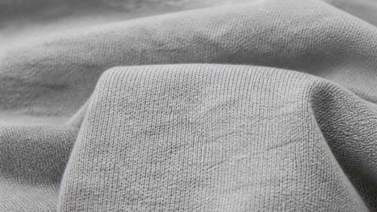 Close-up of high-quality cotton t-shirt fabric showing tight weave structure with visible yarn interlacement and even thread spacing under natural daylight