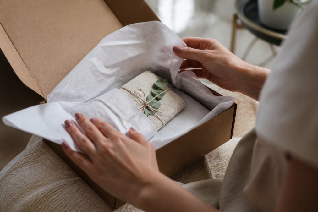 Close-up of hands opening a carefully packaged gift box with protective tissue paper and branded packaging visible