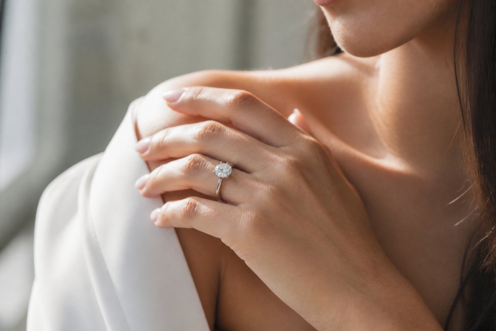 Elegant diamond solitaire ring on a woman's hand with soft natural window lighting, neutral background emphasising the gemstone's sparkle and brilliance, luxury setting