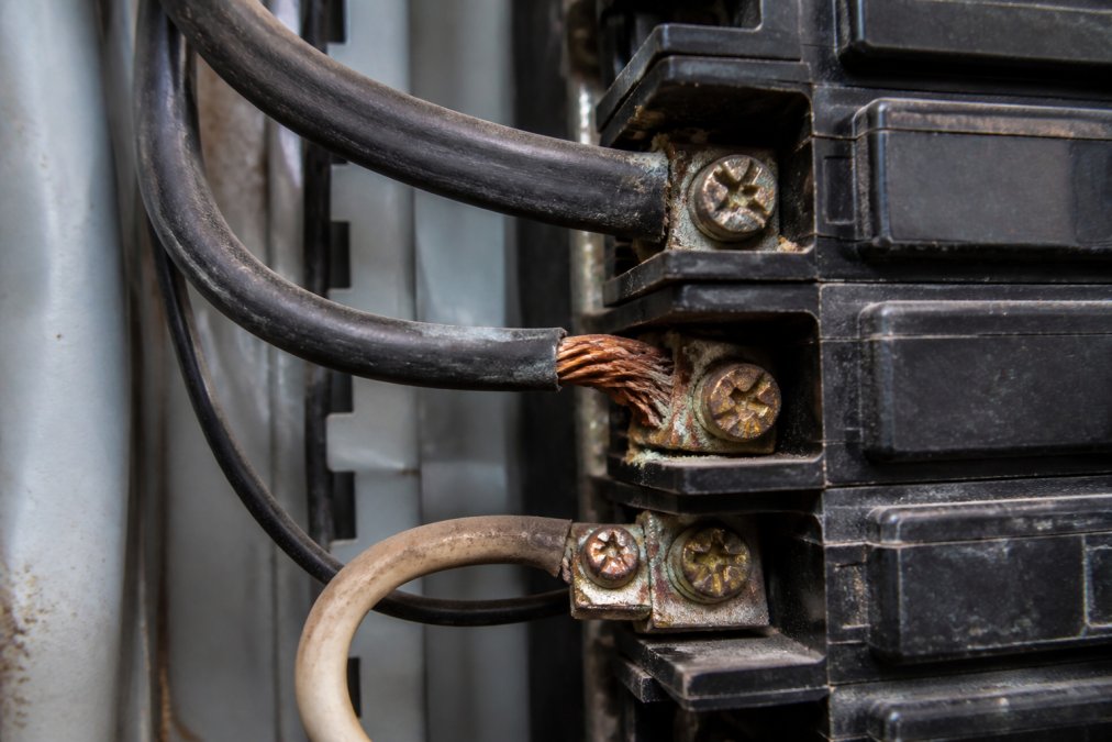 Close-up of an electrical panel showing visible corrosion on breaker terminals, loose wire connections, and discolored copper contacts in a commercial facility