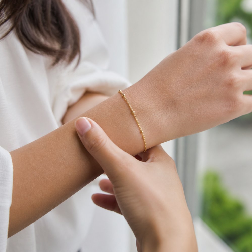 Close-up of a woman's wrist wearing a delicate gold bracelet, soft natural light highlighting the metal against her skin