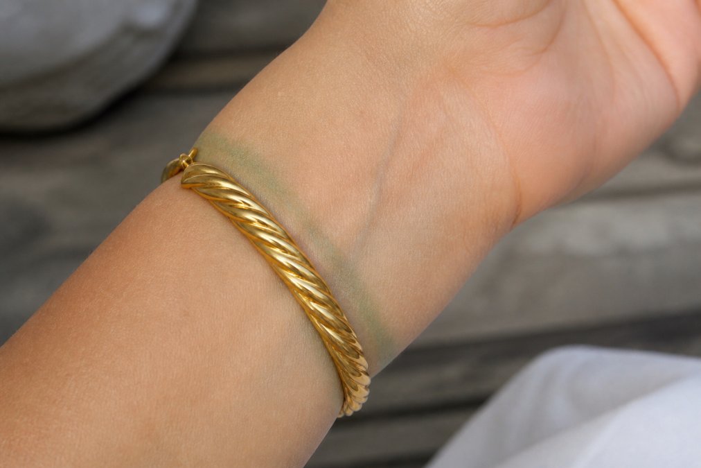 Woman's wrist displaying a gold plated bracelet with visible green discoloration marks around the contact area on her skin