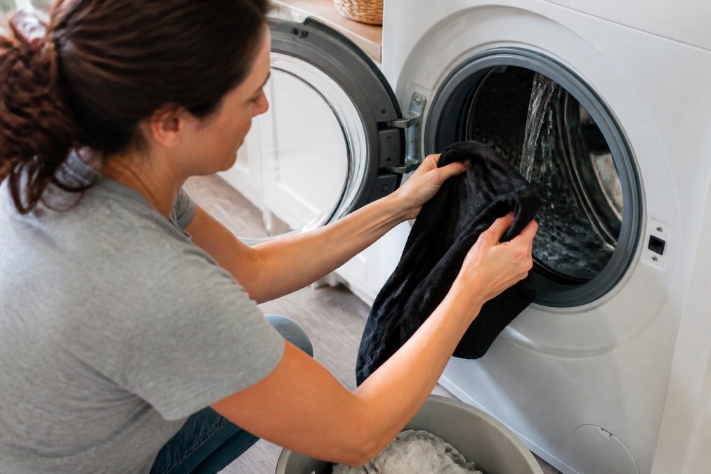Close-up of hands turning a graphic tee inside out before placing it in a washing machine with cold water running