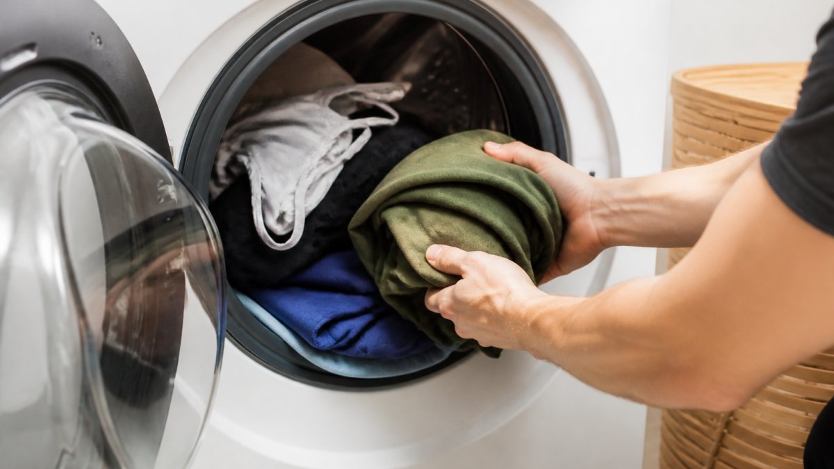 Close-up of gym clothes being placed into a washing machine, showing proper loading technique with colours separated and delicate items on top