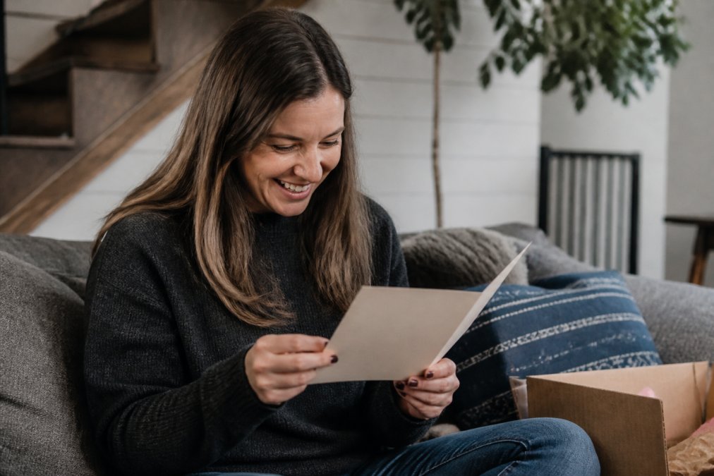 Person opening a handmade greeting card with a genuine smile, showing the moment of emotional connection and authentic reaction to receiving something made by hand