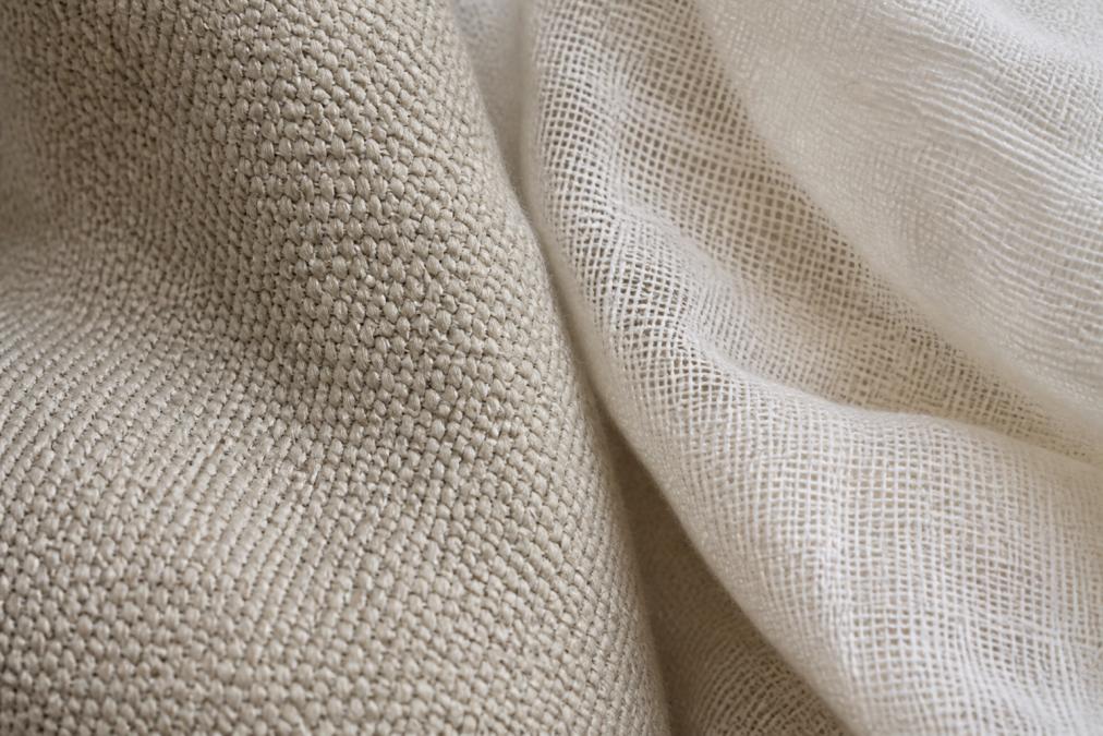 Close-up of tightly woven heavyweight cotton fabric showing dense interlocking fibres with visible texture, contrasted against loosely woven lightweight cotton beside it, natural daylight