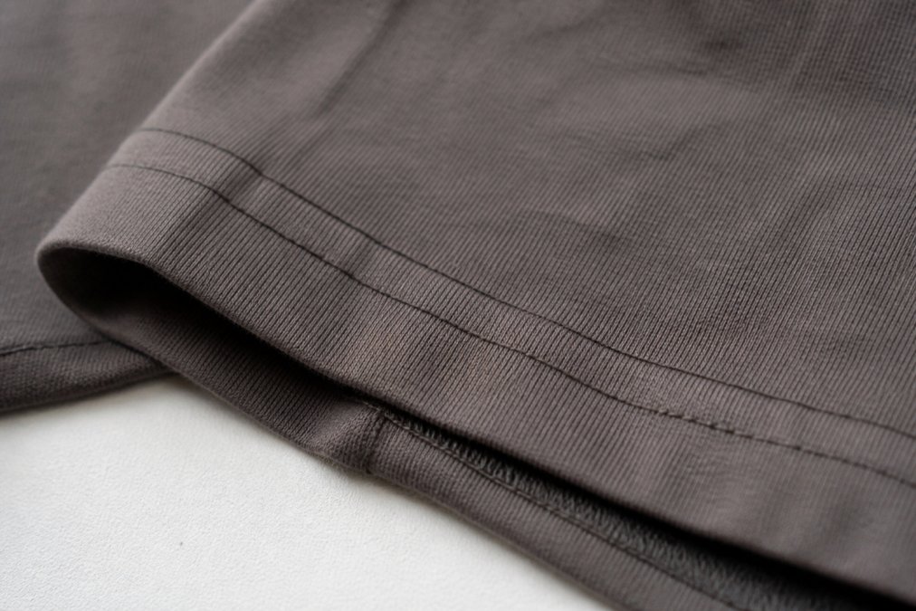 Close-up of double-needle stitching on a heavyweight tee seam, showing reinforced parallel thread lines and quality construction detail with natural lighting