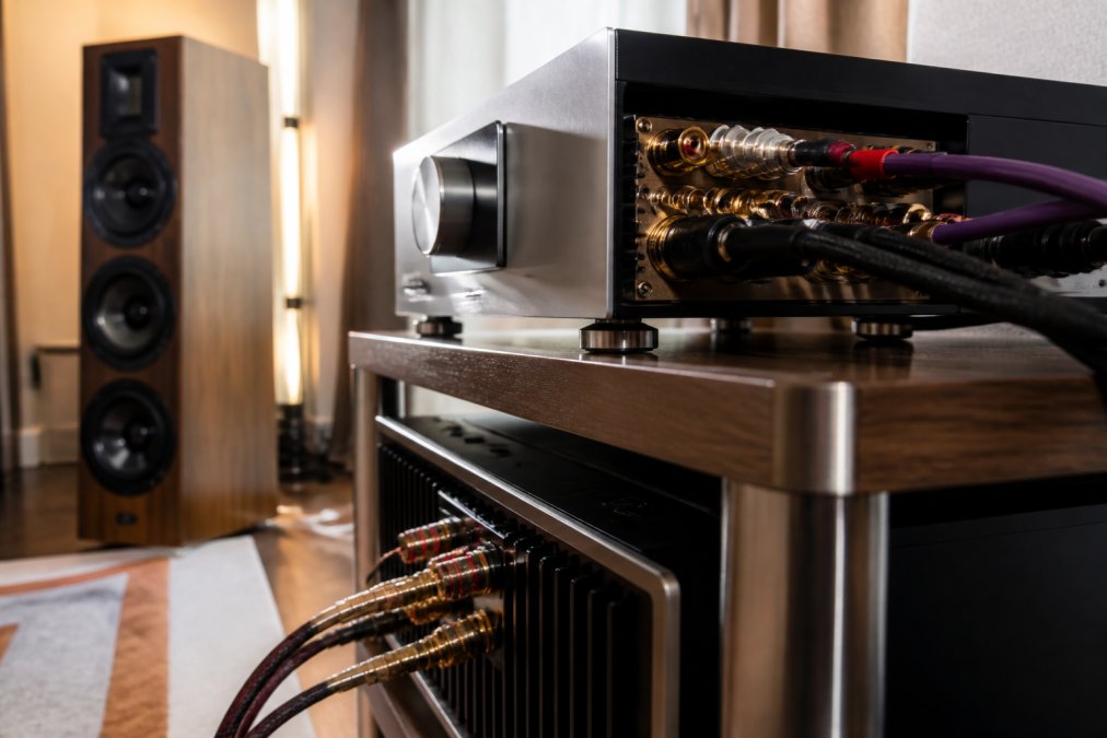 Close-up of high-end audio DAC and amplifier components on a wooden shelf in a warmly lit dedicated listening room, with speaker cables neatly connected