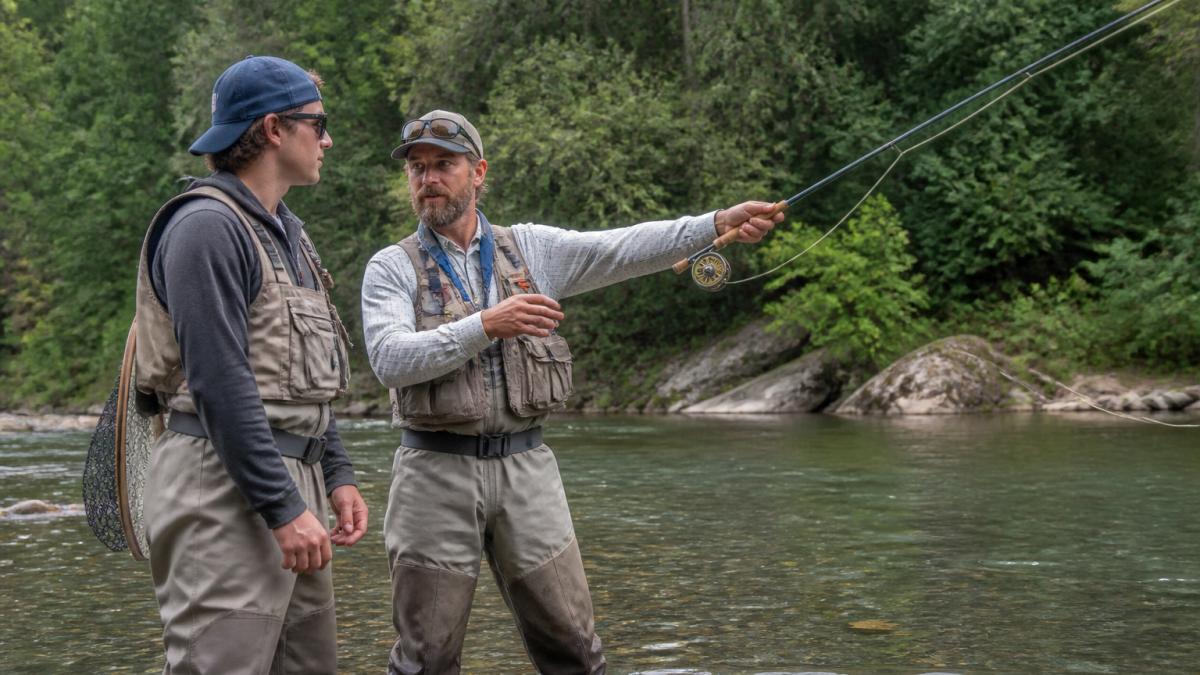Professional fishing guide teaching an angler proper casting technique while standing in a shallow river.