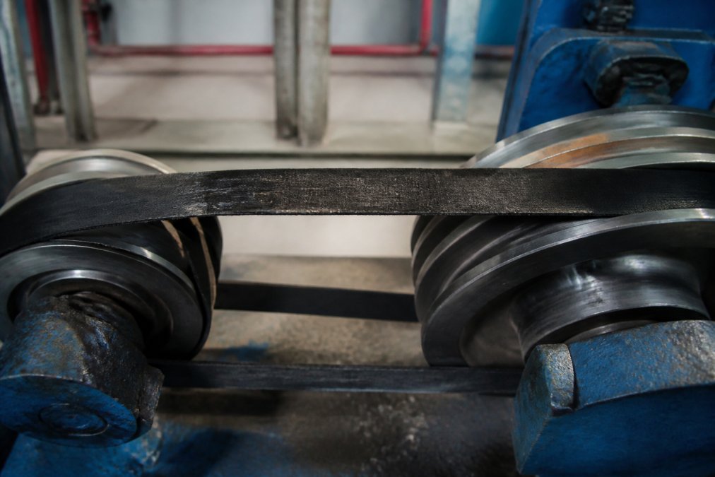 Close-up of misaligned pulleys on an industrial drive system showing visible wear marks on belt sidewalls and uneven contact on sheave grooves under workshop lighting