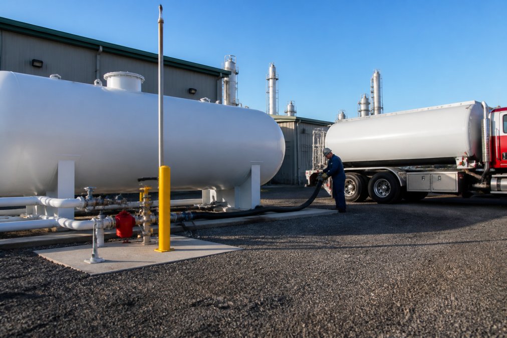A large industrial propane storage tank on a manufacturing facility site with a delivery truck in the background, showing on-site fuel infrastructure
