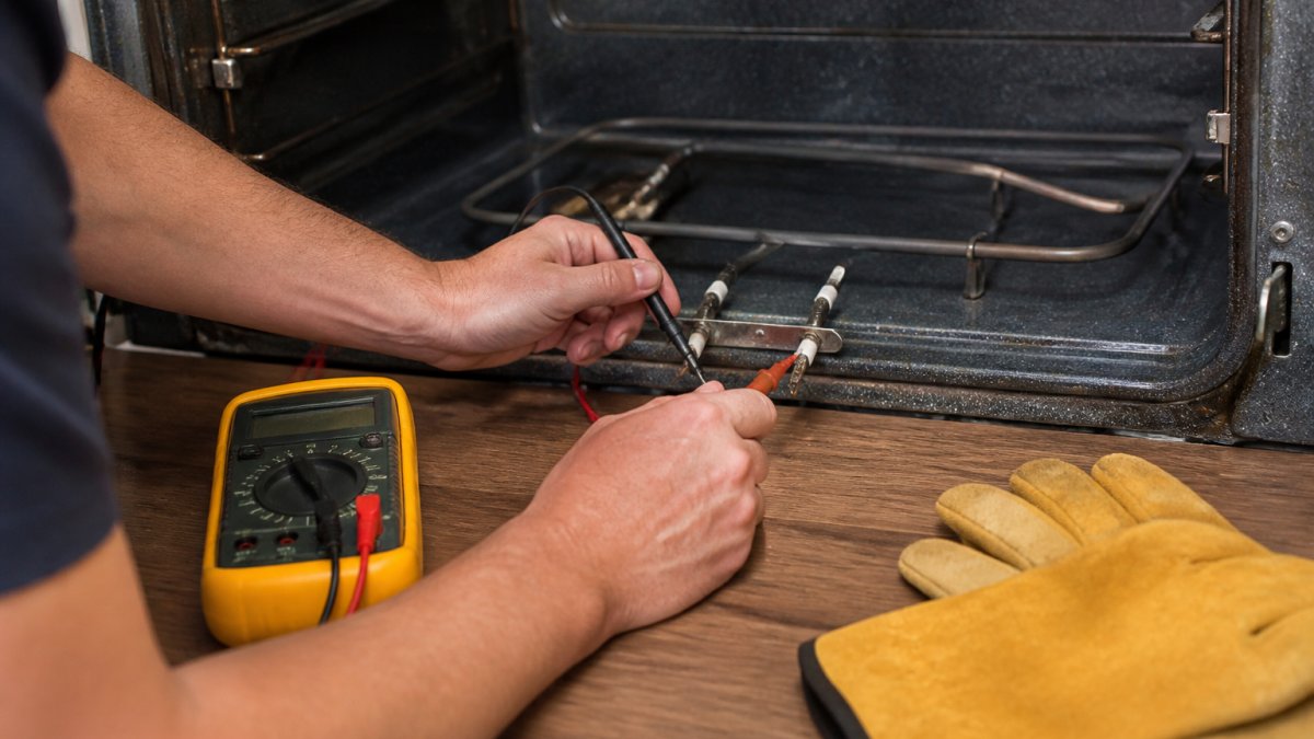 Hands using a multimeter probe to test an oven heating element for continuity