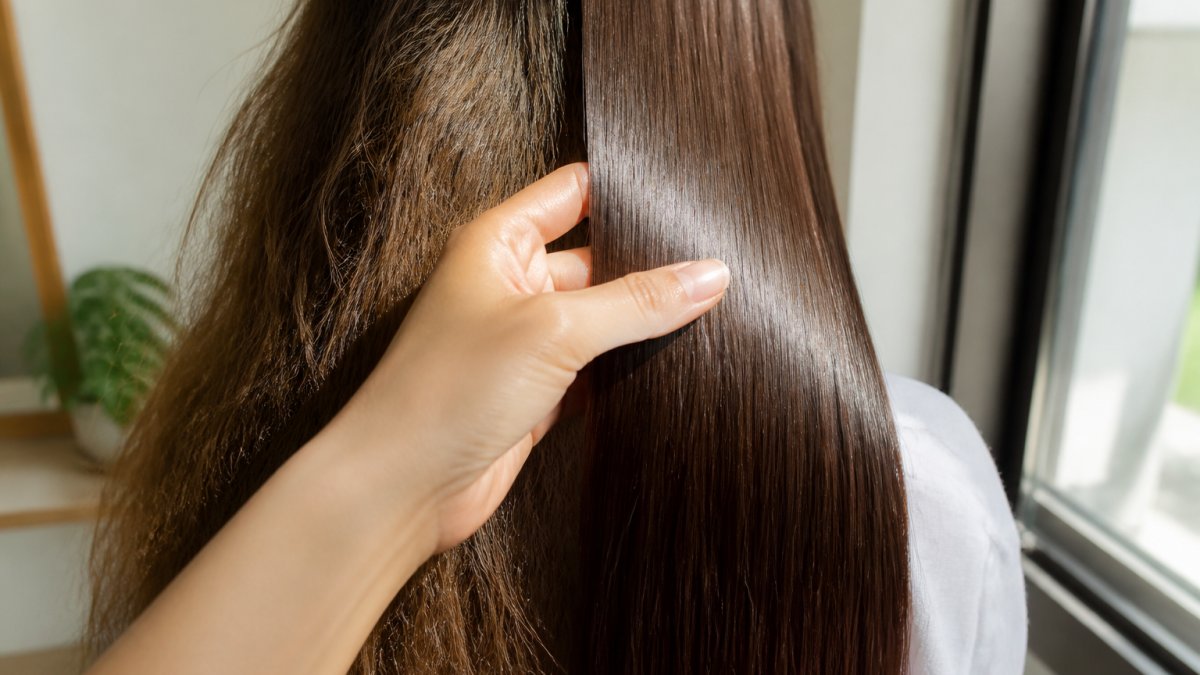 Close-up of a woman's hand running through shiny, smooth hair with visible shine and softness, showing the contrast between treated and untreated sections under natural window lighting