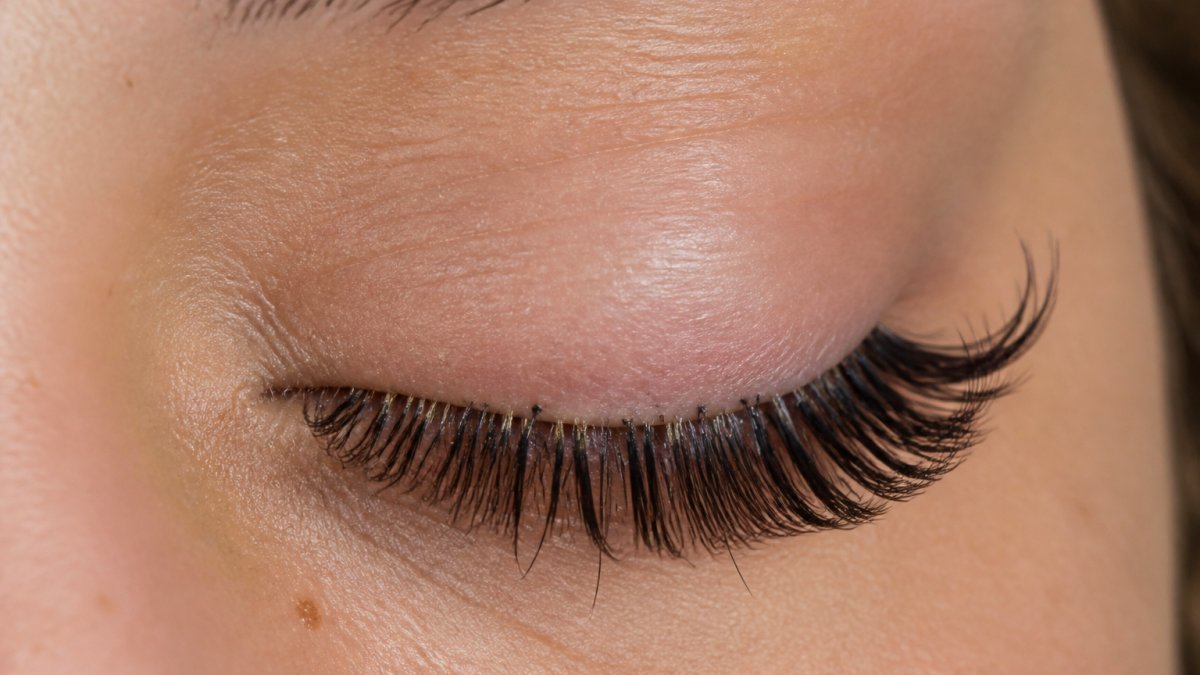Close-up of a person's eye showing lash extensions attached to natural lashes with clear detail of the lash line and extension attachment point in professional lighting