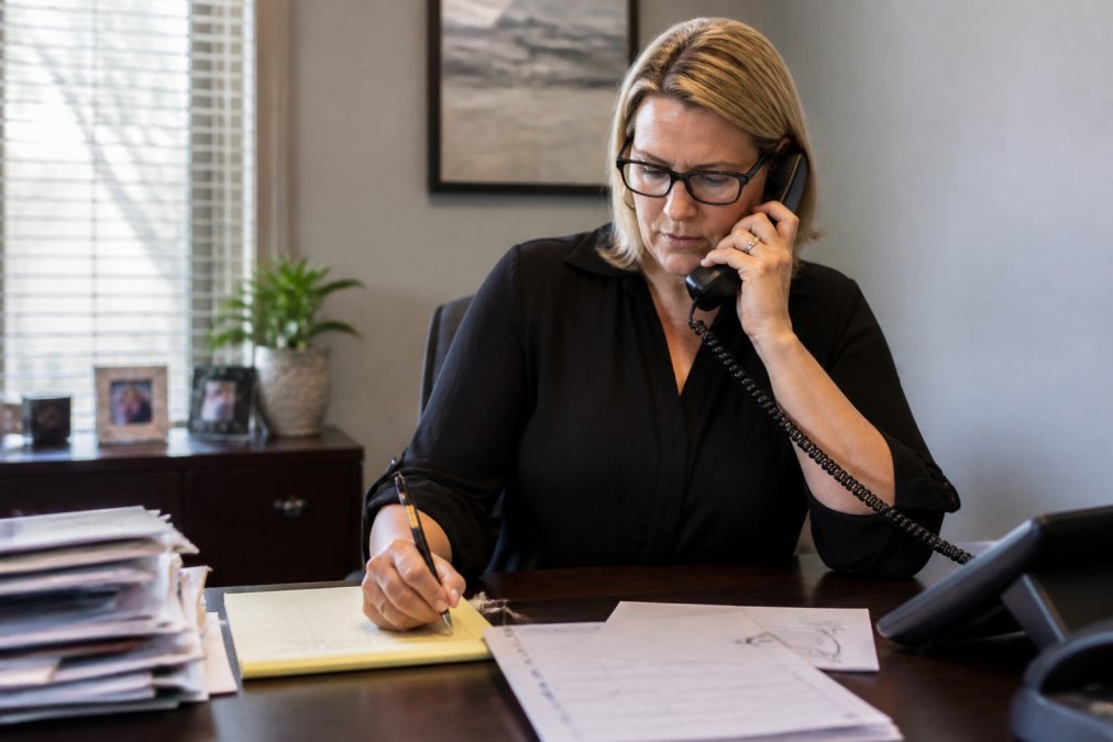 Insurance professional on phone call, taking detailed notes while assisting customer with claim filing or policy question in organized office setting