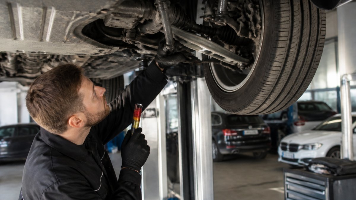 Professional technician examining suspension components on a luxury vehicle lifted on a service bay, using diagnostic equipment to test all-wheel-drive coupling engagement