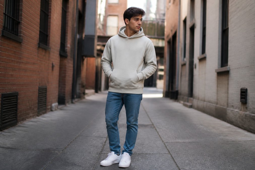 Young adult wearing a minimalist christian streetwear hoodie, jeans, and sneakers in an urban setting