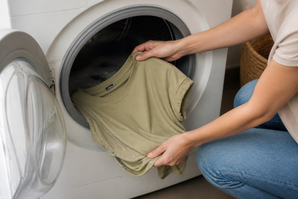 Hands gently placing a modal garment into a washing machine filled with cool water, demonstrating careful handling and proper washing technique with soft natural lighting