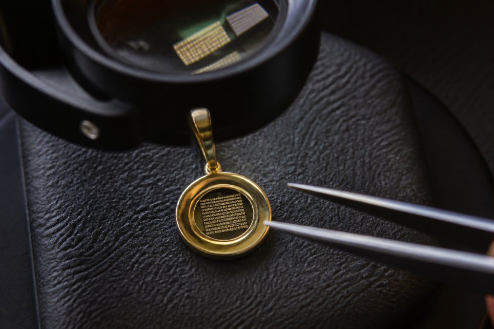 Close-up of a delicate nano-engraved Bible verse pendant displayed on premium materials under professional magnification, showing microscopic detail and crystal-clear legibility of engraved text on the nano chip